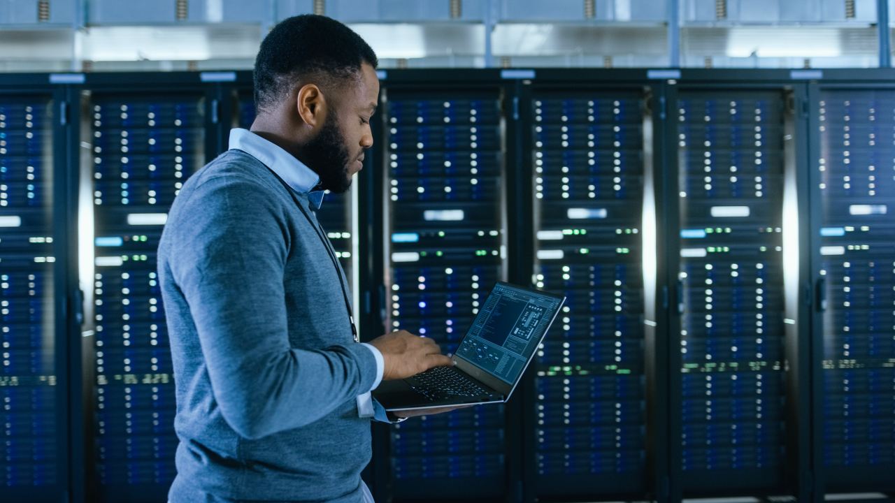 a man working on a laptop in front of server racks in a data center | AI Cluster